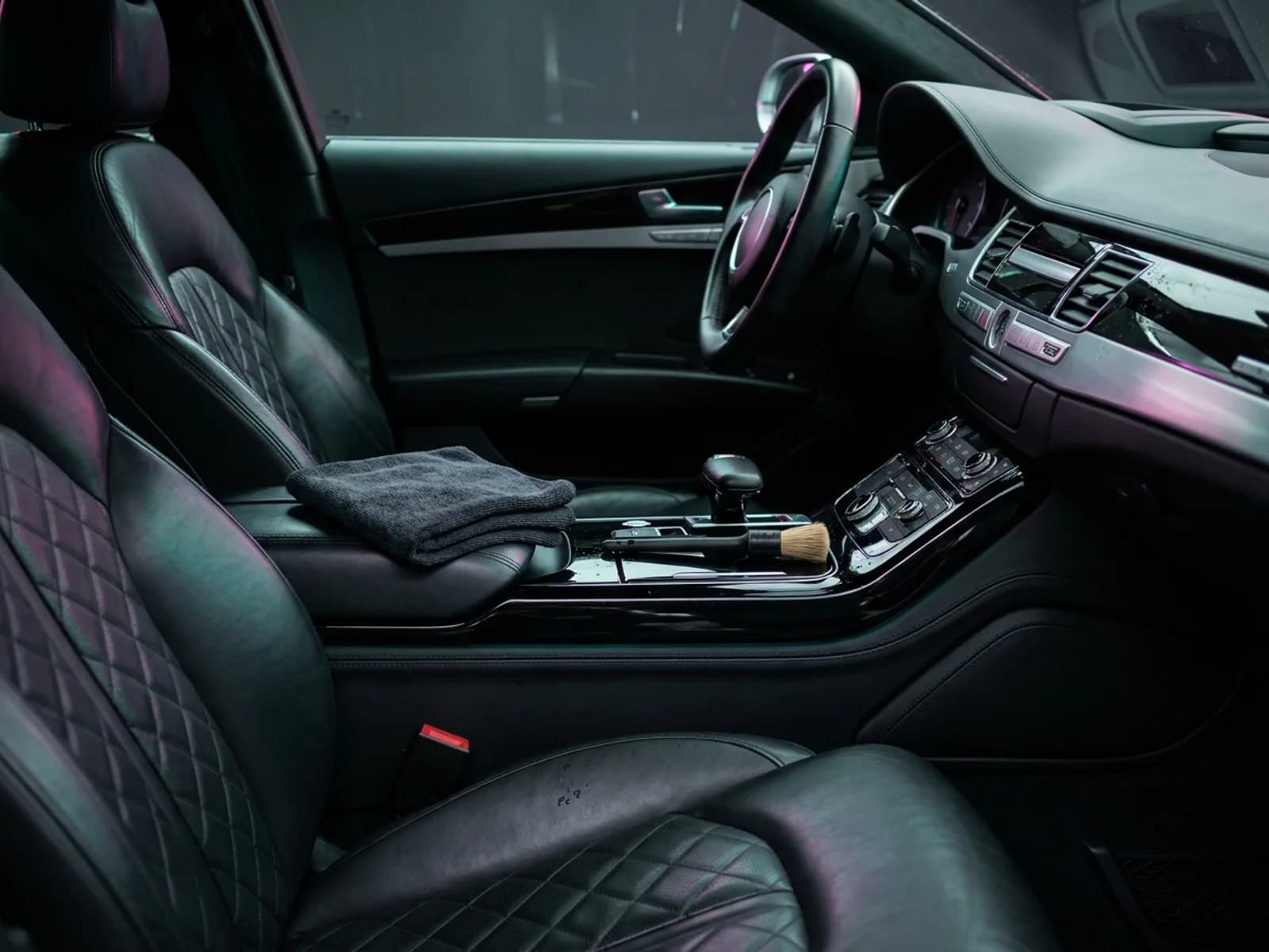 Frisch aufbereiteter Premium-Fahrzeuginnenraum mit makellosem schwarzem Steppleder, Mikrofasertuch und Detailing-Pinsel, Türkis-Magenta-Kantenlicht